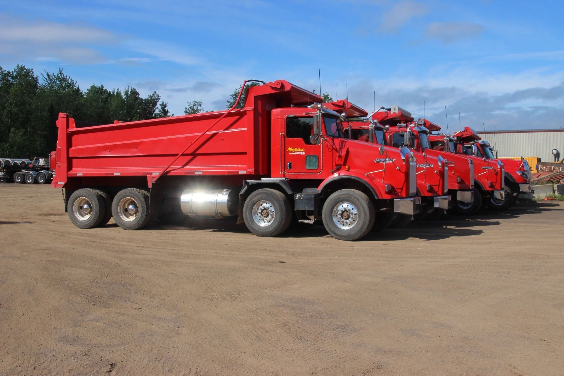 Line of red MacArthur's Kenworth dump trucks parked in the yard